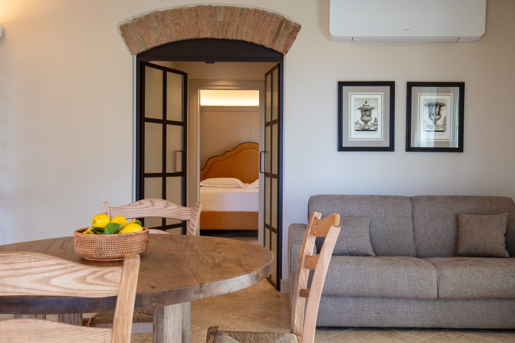 Découvrez l'intérieur de l'Appartement Tramontana. Salon moderne avec canapé gris, table ronde conviviale et accès immédiat à la chambre. Espace optimisé et chaleureux.